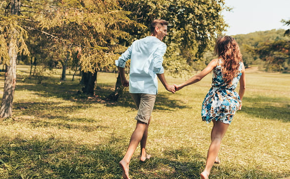 Rear view of romantic couple in love dating outdoors at the park on a sunny day. Happy couple in love walking and playing together on the grass in the nature background. Valentine's day. Couple goals