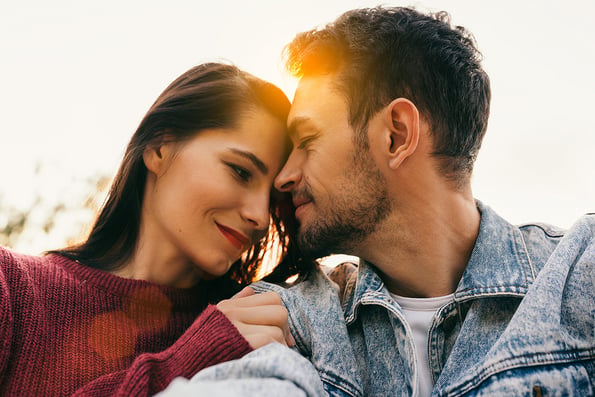 Happy couple in love enjoying sunshine embracing each other looking with love having eyes full of happiness sitting against sky and nature background. Couple making self-portrait on dating day. Family