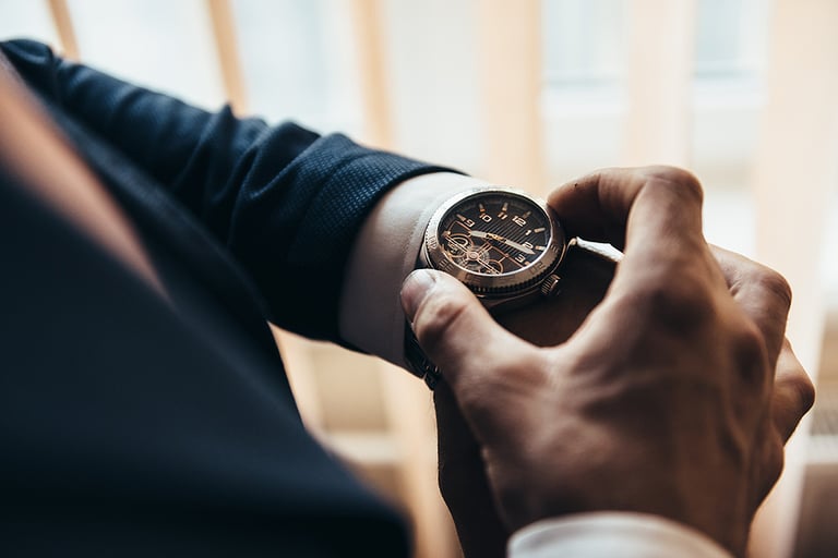 a stylish mechanical watch on the arm of a man dressed in a blue jacket with a white shirt that watches the time on the clock holding the clock by hand