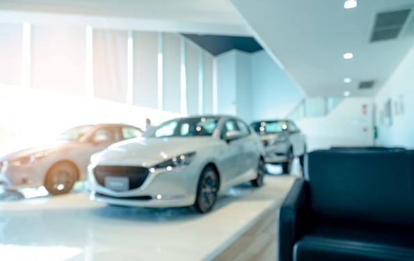 Blurred front view of white car and customer. New luxury car parked in modern showroom. Car dealership office. Electric car business concept. Automobile leasing. Showroom interior building design.
