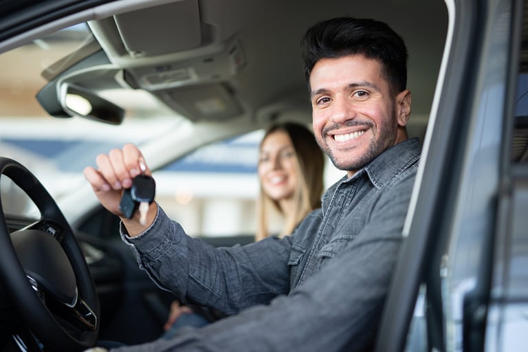 Young happy man showing the key of his new car in a car dealer saloon