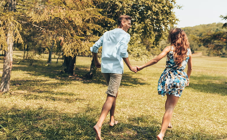 Rear view of romantic couple in love dating outdoors at the park on a sunny day. Happy couple in love walking and playing together on the grass in the nature background. Valentine's day. Couple goals