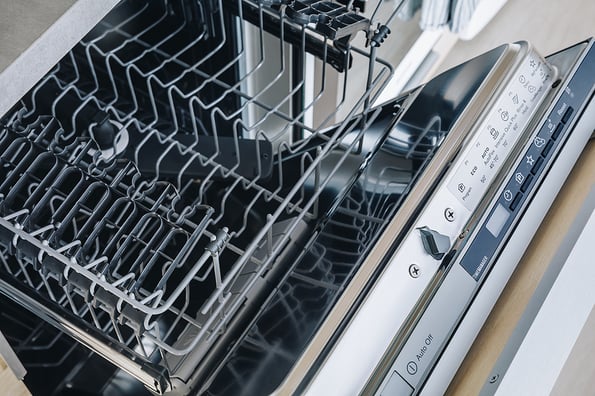 Colorful dishwasher detergent tablet for dishwashing machine. Open dishwasher with clean glasses and dishes close-up in modern kitchen.