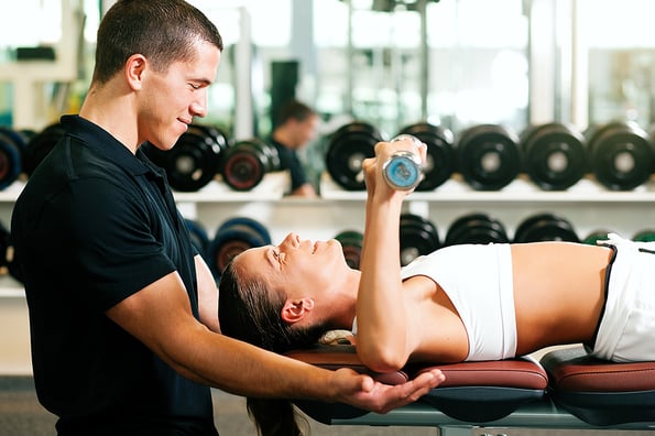 Woman with her personal fitness trainer in the gym exercising with dumbbells
