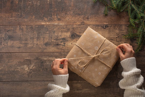 Christmas gift. Congratulations.Top view of woman holding traditional decorated gift box. Hands holding gift box on wooden background. Woman s hands open Christmas gift