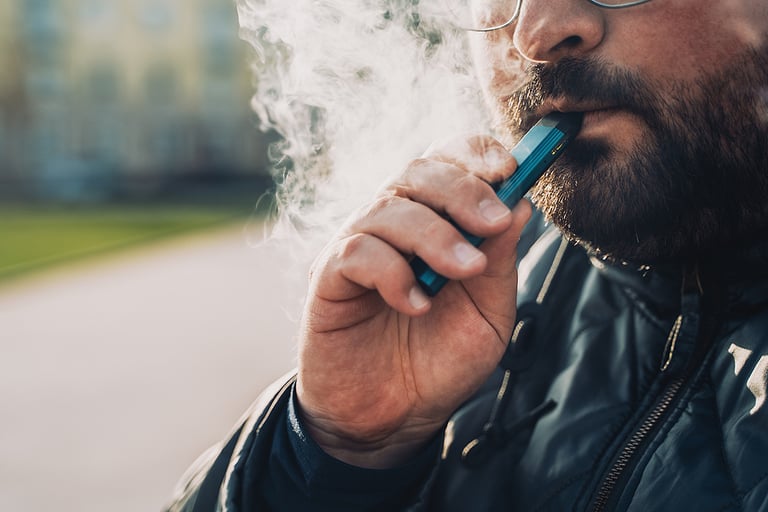 Man smokes new Vape Pod System, inhales and exhales vapor of electronic cigarette, vaping concept, selective focus, toned