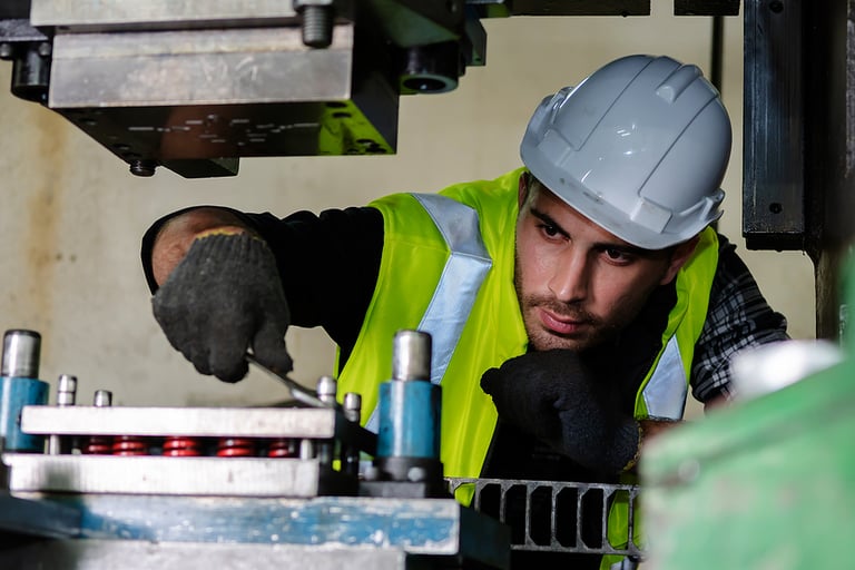 A caucasian male mechanical engineer is checking the machine for metalwork in the factory. An engineer wears a helmet and working on the machine in the metalwork industry.