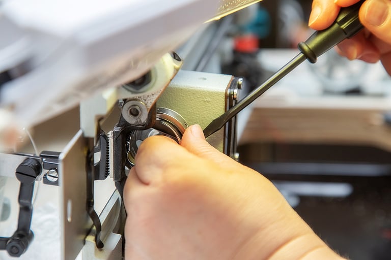 Female hands with a screwdriver repair the shuttle of the sewing machine. Repair of an industrial sewing machine at home. Maintenance.