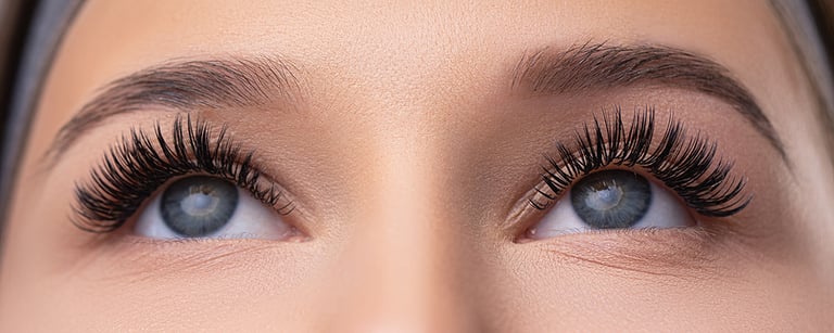 Close up portrait of woman face. Young, beautiful girl with fresh soft skin combing long black eyelashes with special mascara brush. Fake eyelashes. Eyelashes extensions close up