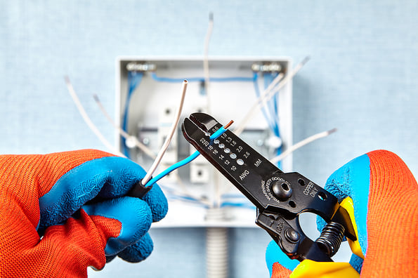 The use of the stripper cutter tool to strip the end of the electrical wire when repairing and updating wiring in the home grid. Electric installation work. Installing new fusebox with circuit breaker electrician