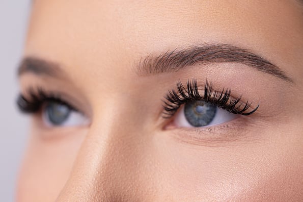 eyelash extensions Close up portrait of woman face. Young, beautiful girl with fresh soft skin combing long black eyelashes with special mascara brush. Fake eyelashes. Eyelashes extensions close up