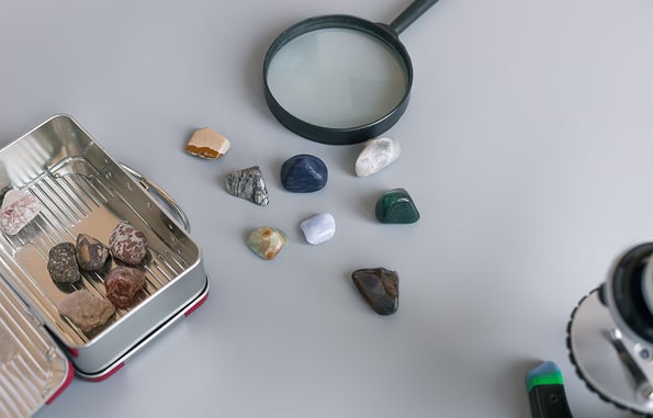 collection of semiprecious stones on gray table with magnifying glass, box and microscope. Mineral stones collection, geology. copy space
