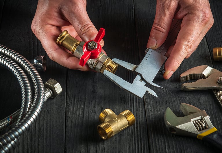 Plumber measures the size of fitting using a caliper before connecting water or gas pipe. Closeup of the hands of the master plumber in workshop.