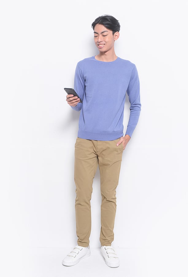 Full size photo of young handsome man wearing blue sweatshirt ,khaki pants ,use cellphone answer sms messages have online conversation. Chino pants.
