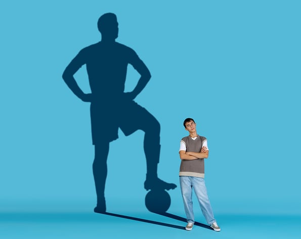 Man dreaming about big and famous sport future. Conceptual image with boy and shadow of football player on blue background. fantasy sports.