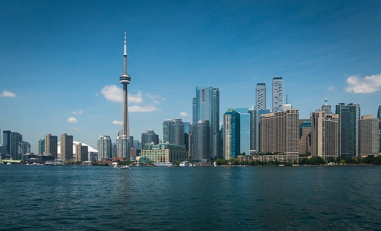 Toronto skyline with scyscrapers and Lake Ontario on beautiful sunny day as seen from Toronto islands. Blue sky, few clouds, early afternoon. Reflections of skyline in water. No people, copyspace.