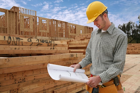 A home contractor holding blueprints outside a home in progress