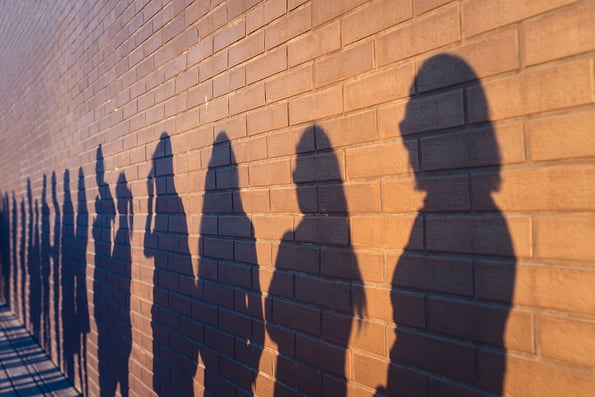 People crowd shadows lined up against a red brick wall. They are in a queue for changes in life. Social distance, covid and immigration issue concept