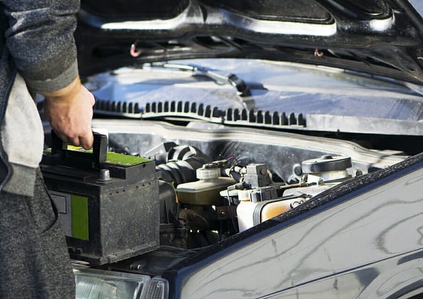 put the battery in the car, auto repair. An auto mechanic is about to put in the battery and tighten a new car battery nut in a car workshop. black car. new battery in the hands of the mechanic