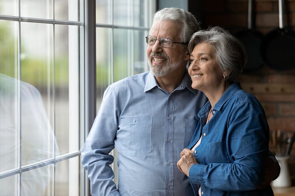 Happy bonding loving middle aged couple looking out of window.