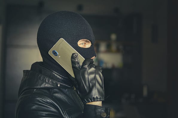 Young adult in black clothes with hidden face. Ill-intended fraudster uses mobile. Fraudster calls. Mobile racket. Hacker hijacks by phone. Cellphone account fraud. Scam