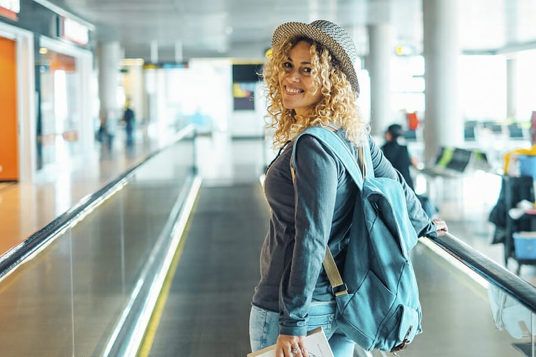 Cheerful young adult woman travel at the airport with backpack. Female people portrait smiling and walking at the gate. Pretty blonde lady traveler enjoy trip and holiday vacation leisure activity