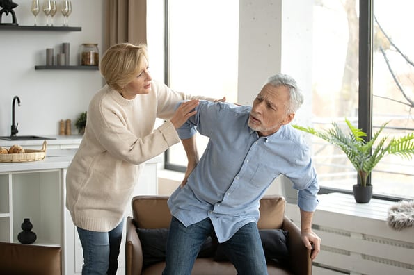 Concept of health problems. Worried woman support her husband with pain in lower, care and help him to sit in armchair. Senior man with chronic ache, injury and muscle inflammation