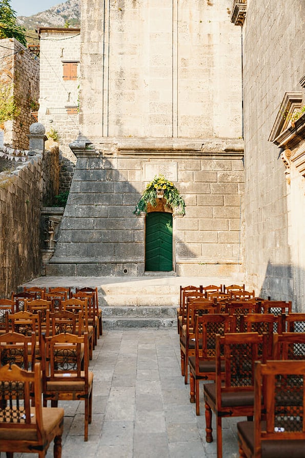 Wooden chairs with patterns on the backs stand in rows on the cobblestones in front of the church door