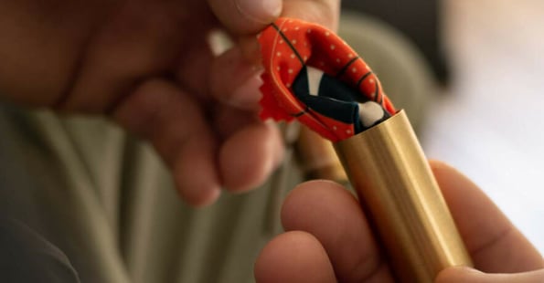 Person removing a glasses cleaning cloth from a small metal tube