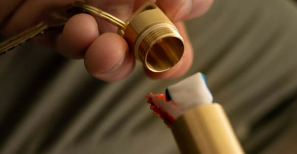 Person opening a brass keyring tube containing an orange glasses cleaning cloth