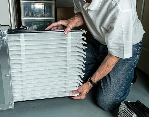 Senior caucasian man checking a clean folded air filter in the HVAC furnace system in basement of home