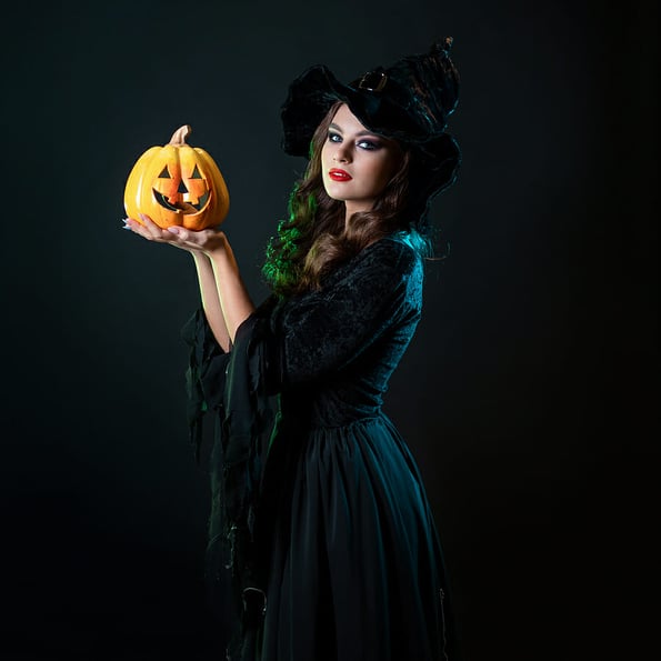beautiful witch in a pointed hat Holding a pumpkin with a laughing face, Jack lantern. Halloween party, witches Sabbath. Young beautiful brunette in witch costume,