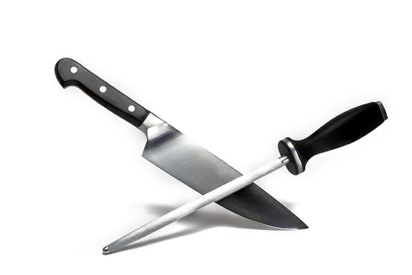 Close up of a high quality large sharp meat kitchen knife crossed with a long grinding stick both with black handle on white background concept for knife sharpening and sharp knives