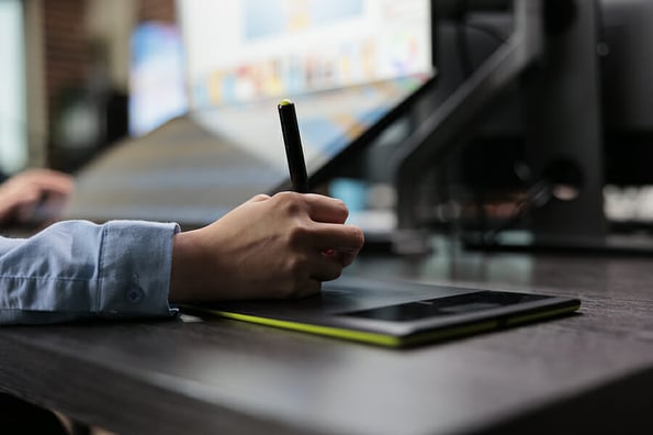 Closeup of creative graphic designer using stylus pen and graphic tablet to edit photos. Digital photo editor sitting at desk with multiple displays while using editing software to retouch images.