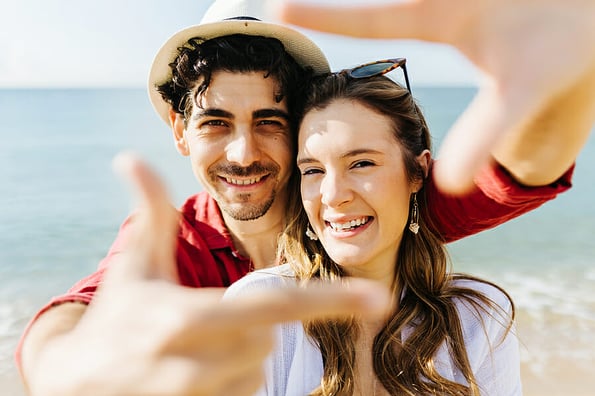Happy couple enjoying summer vacation on the beach - Man making photo frame with his hands while posing with his girlfriend on the beach - Vacation and relationship concept.