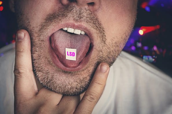 Close-up on junkie young man is taking LSD. guy swallows puts a brand of narcotic acid on his tongue against background of a concert in a club. Junkies have fun at night on raver party at a nightclub.