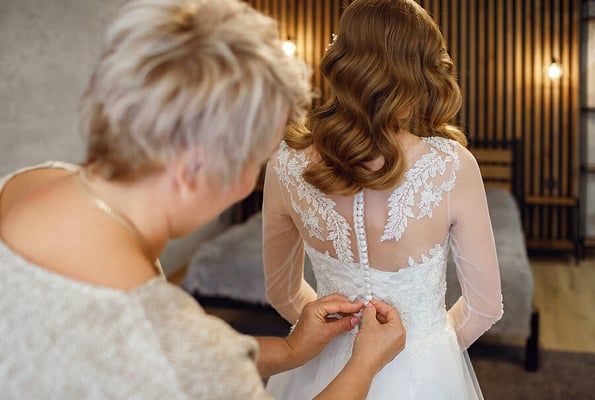 On the wedding day, mom helps her daughter put on the bride's wedding dress. A beautiful young woman is preparing to marry her husband