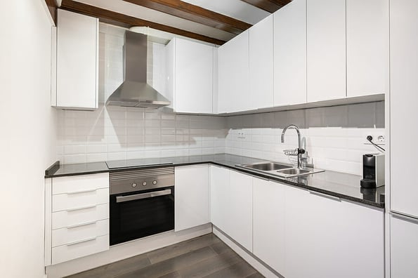 Modern light kitchen in a classic style with white wood corner cabinets, glossy dark marble countertops and white wall tiles. Kitchen appliances and fittings made of stainless steel.
