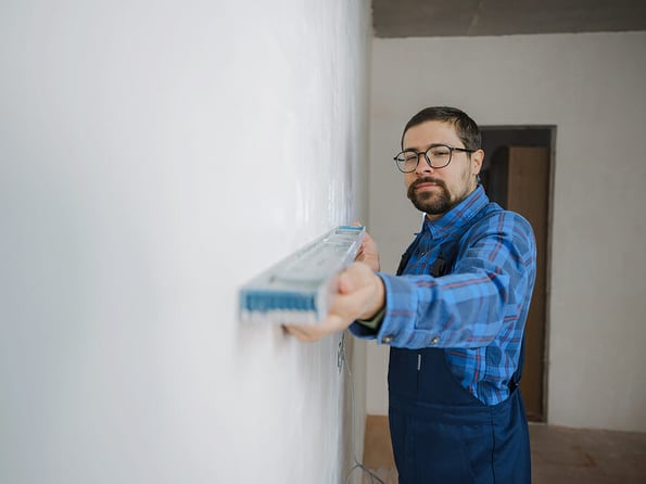 young man in blue work suit doing Repair apartment. Home renovation concept. Cropped shot of handsome bearded young man holding level tool during home improvement