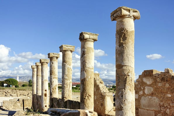 PAPHOS, CYPRUS - January 29 2023: Columns and structures are part of the ancient romans ruins in Paphos Archaeological Park - Cyprus. At the background the lighthouse This site is an UNESCO World Heritage site