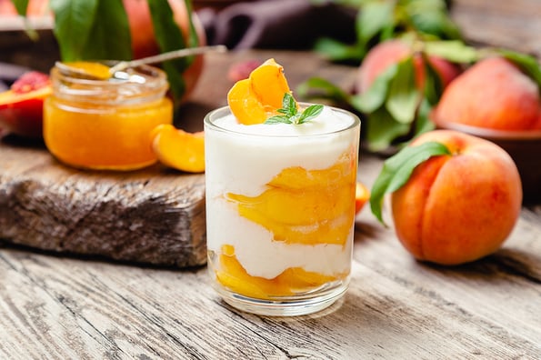 Peach fruit dessert in glass cup on rustic wooden table with fresh peach fruit, peach jam. Homemade dessert with fruits. Fruit salad with yogurt or sour cream.