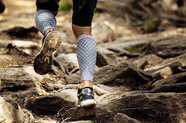 athlete runner runs rocks in mountain. closeup of legs compression socks and sneakers