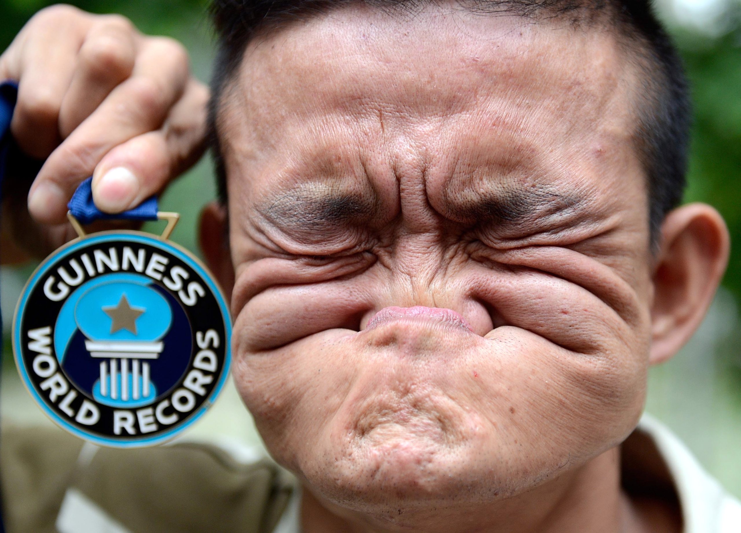 Chinese performer Tang Shuquan shows his Guiness World Records medal while biting his nose on a street in Chengdu city, southwest Chinas Sichuan province, 5 June 2012