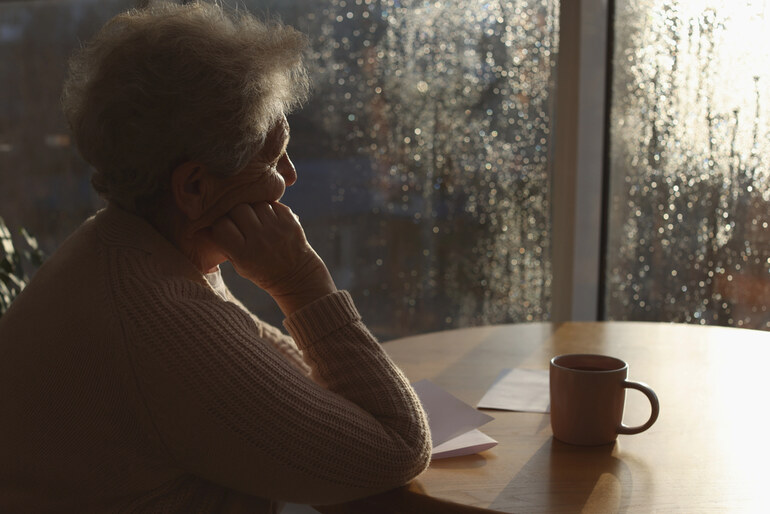 Woman Sitting with a Cup of Tea by a Window, Reflecting on Adult Loneliness and Mental Health Awareness.