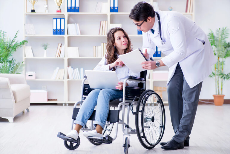Doctor reviewing documents with a wheelchair user during a medical consultation after an unexpected injury.