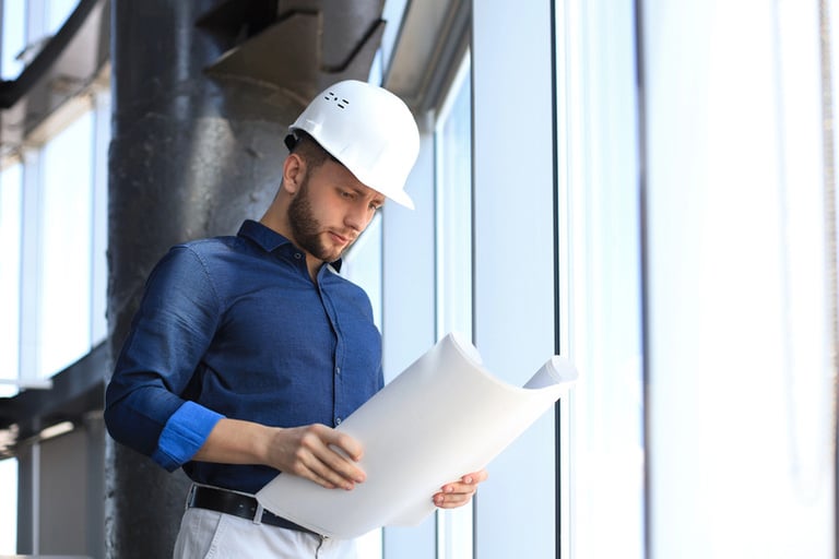 An engineer in a hard hat is reviewing construction blueprints, illustrating the process of evaluating a metal building quote and project specifications.