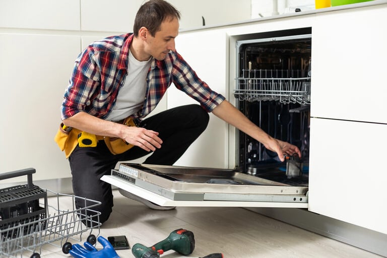 A man sitting on the floor carefully cleaning the coils of a refrigerator, focusing on proper maintenance to improve appliance efficiency and performance.