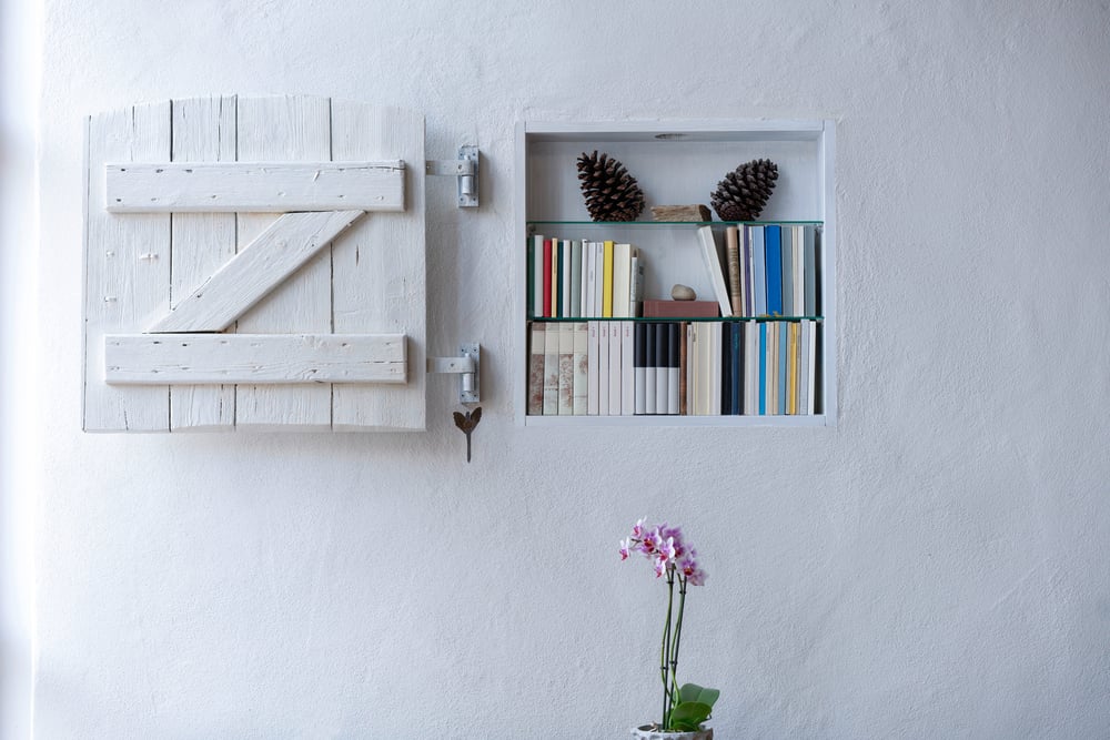 Small white bookcase beside a decorative shutter in a compact room