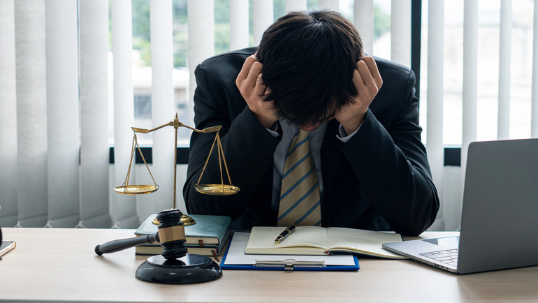 Stressed individual sitting at a desk with legal documents, a judge's gavel, and scales of justice, illustrating practical ways to reduce stress while navigating a legal case.