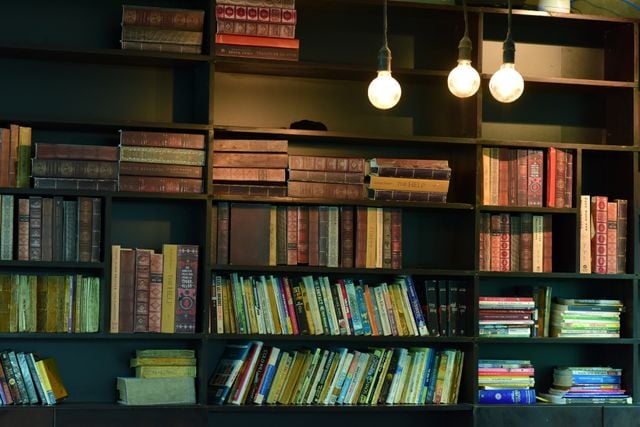 A vintage-style painted bookshelf filled with classic and colorful books under warm lighting.